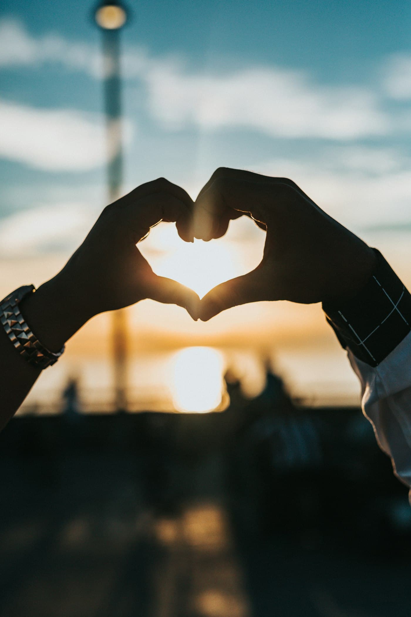Two people forming a heart shape with their hands at sunset
